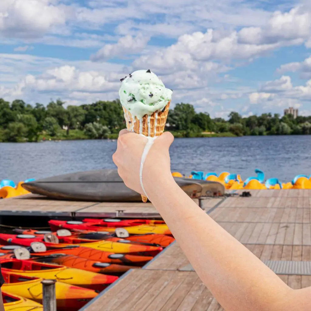 Hand holding up ice cream cone while it slowly melts. Background of Como Lake and dock with kayaks